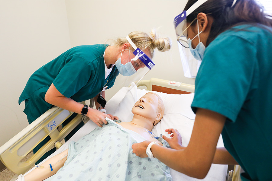 Students performing diagnostics on nursing mannequin