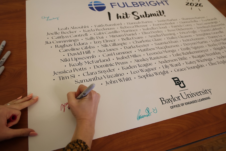 A student signs her name on the Fulbright applicant poster at the I Hit Submit! event